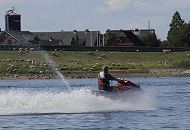 17_21610 Ein Jetski fhrt in hohem Tempo auf der Elbe; das Wassermotorrad hinterlsst eine dichte Spur von Gischt. Freunde dieses lauten Wassersports bentigen einen Sportbootfhrerschein Binnen oder See, da die Jetboote mehr als 5 PS Motorleistung haben. Sie erreichen eine Geschwindigkeit von ca. 120 km/h und haben eine Maschinenleistung von 150 und mehr PS. Im Hintergrund steht eine Schafherde verteilt auf dem Elbdeich und grast - die Schafe halten nicht nur das Gras auf dem Deich kurz, sie treten auch den Boden fest. www.hamburg-fotograf.com