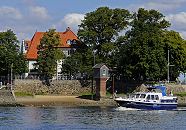 17_21612 Eine Motoryacht fhrt auf der Elbe flussabwrts - der Freizeitkapitn sitzt unter dem Persenning-Sonnenschutz im Fhrerstand des Motorboots. Das Boot passiert gerade das Zollenspieker Fhrhaus und das Pegelhaus am Ufer der Elbe. www.hamburg-fotograf.com