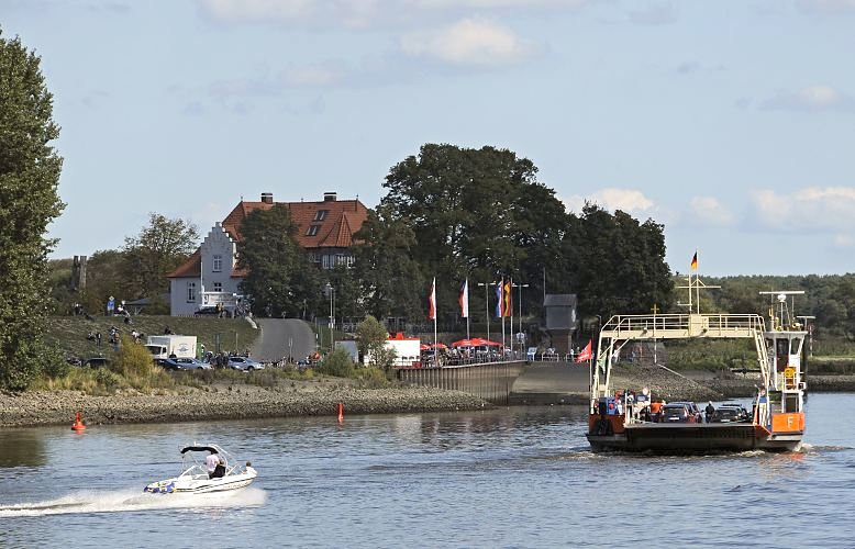 Die Fähre verbindet den Zollenspieker auf der Hamburger Seite der Elbe mit dem Ort Hoopte in Niedersachsen. Die Elbe ist die Grenze zwischen den beiden deutschen Bundesländern. Die Autofähre fährt vom 1. März bis 30. November - sie überquert gerade den Fluss und steuert mit PKW und Fussgängern an Bord den Fähranleger beim Zollenspieker an. Ein Motorboot hat seine Fahrt verlangsamt und lässt das Fährschiff kreuzen. Hinter den Bäumen das Zollenspieker Fährhaus. Bilder aus den Vierlanden - Hamburg Bergedorf, Kirchwerder - Autofähre Zollenspieker Hoopte