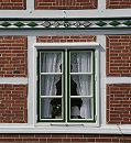 17_21631 Holzfenster in einem Fachwerkhaus; die Gardinen sind mit Spitzen versehen. Der Balken über dem Fenster ist mit farbig abgesetzten Schnitzereien versehen. ©www.hamburg-fotograf.com
