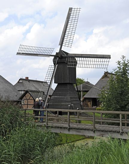 Fotografie Windmhle - Feldentwsserung Vierlande Feldentwsserungsmhle am Entwsserungsgraben im Freilichtmuseum Rieck-Haus. Eine Holzbrcke fhrt ber den Graben, Schilf und Gras wachsen am Ufer. Die Windmhle stand frher in Ochsenwerder und wurde 1952 zum Freilichtmuseum Curslack gebracht