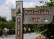 17_21637 Handgeschnitztes Hinweisschild zum Mhlenladen und Cafe bei der Riepenburger Mhle. Auf der Strassen fahren Inlineskater und ein Fahrrad. Die Strassen durch die Drfer der Vier- und Marschlande werden am Wochenende hufig von den Hamburger Ausflglern fr dieses sportliche Freizeitvergngen genutzt. www.hamburg-fotograf.com