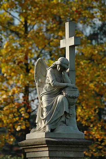 Foto Friedhof -  St. Johannis Neuengamme Trauernder Engel mit Kreuz auf dem Friedhof der St. Johanniskirche in Neuengamme, Vierlande. Der Trauerengel mit Flgel sttzt seinen Kopf mit der Hand und blickt nach unten. Im Hinter- grund die leuchtenden Farben Gelb und Rotbraun der Bume im Herbst.  