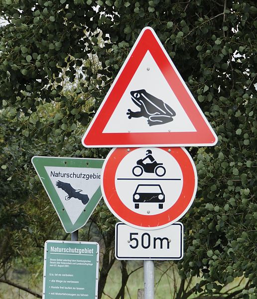 Foto von Schildern, Naturschutzgebiet / Krtenwanderung Hinweisschild, dass ein Naturschutzgebiet beginnt - zum Schutz der Lebensrume gefhrdeter Tier- und Pflanzenarten drfen nur die ausgewiesenen Wege benutzt werden. Ein weiteres Schild weist auf die Mglichkeit von Krtenwanderung hin; jedes Frhjahr beginnen die Molche, Frschen und Krten ihre Laichwanderung zu ihren Laichgebieten; fr Autos und Motorrder ist die Zufahrt gesperrt.