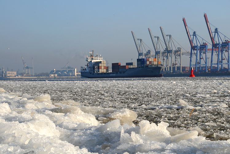 Fotos vom Hamburger Winter Eisschollen auf der Elbe - Containerschiff. 005_22734 Dichtes Treibeis auf der Elbe und am Ufer vor Hamburg Oevelgoenne. Das beladene britische Containerschiff Maike D. fhrt flussabwrts durch das Eis. Die Containerbrcken am Athabaskakai des Container Terminals Burchardkai sind hochgefahren - eine signalrote Tonne begrenzt die Fahrrinne fr die Schiffe auf der Elbe.