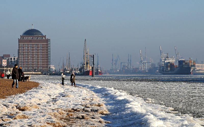 Fotos vom Hamburger Winter - Spaziergnger in der Wintersonne an der Elbe.005_22735 Spaziergnger genieen die Wintersonne am Elbstrand vor Hamburg Neumhlen. Im Hintergrund das ehemalige Khlhaus das zur Seniorenresidenz umgebaut wurde und der  Museumshafen von Oevelgoenne.