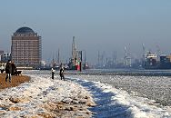 005_22735 Spaziergnger genieen die Wintersonne am Elbstrand vor Hamburg Neumhlen. Im Hintergrund das ehemalige Khlhaus das zur Seniorenresidenz umgebaut wurde und der  Museumshafen von Oevelgoenne. 