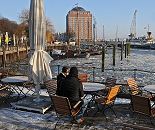 008_22738 Bei sonnigem Hamburger Winterwetter sitzen Gste im Caf am Museumshafen Oevelgoenne. Im Hintergrund das ehem. Khlhaus von Hamburg Neumhlen, das jetzt als Seniorenresidenz seinen Einwohnern einen interessanten Blick ber Elbe bietet.