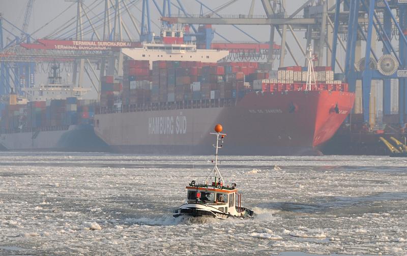 04_5372 Eine Barkasse berquert die Elbe durch den dichten Eisgang des Flusses. Im Dunst liegt der Containerfrachter RIO DE JANEIRO der Reederei Hamburg Sd am Terminal Burchardkai. Das 2008 gebaute Containerschiff kann 5900 TEU / Standart- container an Bord nehmen. Der 286 m lange Frachter kann bei einem max. Tiefgang von 13,5 m eine Geschwindigkeit von 23,0 kn erreichen. Winterimpressionen aus Hamburg - Eine Barkasse fhrt durch das Eis der Hamburger Elbe. 