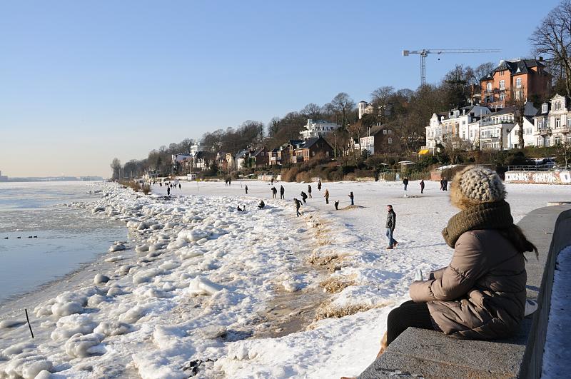 07_5730 Die Wintersonne scheint in Hamburg - Spaziergnger genieen das sonnige Wetter beim Spaziergang an der Elbe. Der Elbstrand ist mit Eis bedeckt, Kinder spielen am Ufer des Flusses. Am Hang stehen die Wohnhuser von Hamburg Oevelgoenne. Hamburg Motive von den Jahreszeiten - Hamburger Winter, Spaziergnger am Elbufer. 