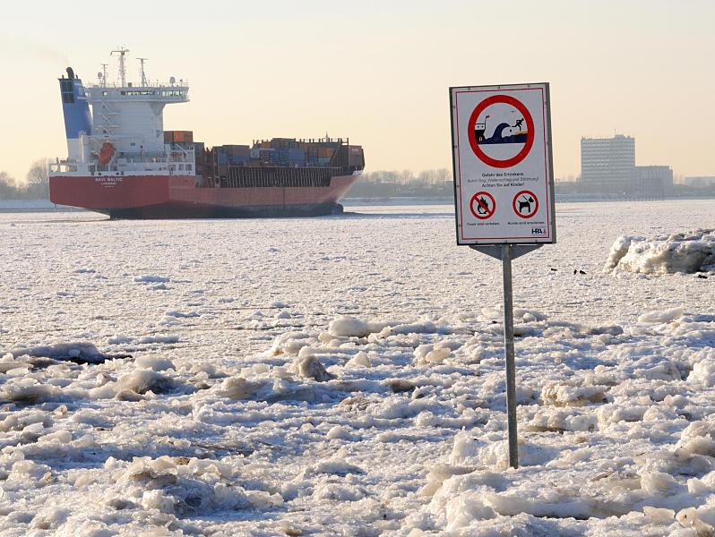 09_5784 Zwischen dem Eis steht am Elbstrand ein Warnschild, das auf Wellenschlag und Sog sowie auf die Gefahr des Ertrinkens hinweist. Der Container Feeder NAVI BALTIC hat den Hamburger Hafen verlassen und fhrt elbabwrts durch das Treibeis.  Fotos von den Jahreszeiten in Hamburg - Winter an der Elbe, Frachtschiff im Elbeis.