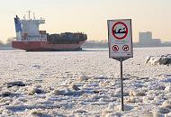 09_5784 Zwischen dem Eis steht am Elbstrand ein Warnschild, das auf Wellenschlag und Sog sowie auf die Gefahr des Ertrinkens hinweist. Der Container Feeder NAVI BALTIC hat den Hamburger Hafen verlassen und fhrt elbabwrts durch das Treibeis.  Fotos von den Jahreszeiten in Hamburg - Winter an der Elbe, Frachtschiff im Elbeis.