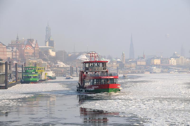 12_5327 Die Elbfhre REEPERBAHN bahnt sich ihren Weg durch das dichte Treibeis auf der Elbe - im Hintergrund das typische Hamburg Panorama mit den unterschiedlichen Kirchtrmen im Dunst des Winternachmittags.  Winter in der Hafenstadt Hamburg -  Panorama der Hansestadt im winterlichen Dunst. 