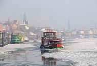 12_5327 Die Elbfhre REEPERBAHN bahnt sich ihren Weg durch das dichte Treibeis auf der Elbe - im Hintergrund das typische Hamburg Panorama mit den unterschiedlichen Kirchtrmen im Dunst des Winternachmittags.  Winter in der Hafenstadt Hamburg -  Panorama der Hansestadt im winterlichen Dunst. 