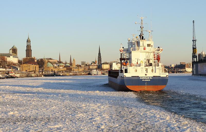 14_5837 Die Elbe vor den andungsbrcken ist dicht mit Treibeis bedeckt. Das Frachtschiff CAROLIN G. bahnt sich seinen Weg durch die Eisschollen, um seinen Liegeplatz im Hamburger Hafen zu erreichen. Im Hintergrund das Hamburger Panorama mit den Sandsteingebuden der Landungsbrcken, dem kupfergedeckten Kuppelgebude des Alten Elbtunnels und den Kirchtrmen von vier der fnf Hamburger Hauptkirchen. Panorama der Hansestadt Hamburg im Winter -  Kirchtrme der Hamburger Hauptkirchen.