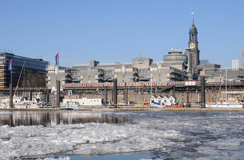 16_5628 Blick ber den eisbedeckten Niederhafen und Sportboothafen am Baumwall Richtung St. Michaeliskirche, eine der fnf Hauptkirchen Hamburg. Das Hamburger Wahrzeichen wird im Volksmund liebevoll " Michel" genannt. Vor dem Verlagsgebude der Gruner + Jahr AG fhrt ein Hochbahnzug zur Haltestelle Baumwall. Hamburger Wintermotive - Eis im Niederhafen - Turm der St. Michaeliskirche. 