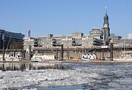 16_5628 Blick ber den eisbedeckten Niederhafen und Sportboothafen am Baumwall Richtung St. Michaeliskirche, eine der fnf Hauptkirchen Hamburg. Das Hamburger Wahrzeichen wird im Volksmund liebevoll " Michel" genannt. Vor dem Verlagsgebude der Gruner + Jahr AG fhrt ein Hochbahnzug zur Haltestelle Baumwall. Hamburger Wintermotive - Eis im Niederhafen - Turm der St. Michaeliskirche. 