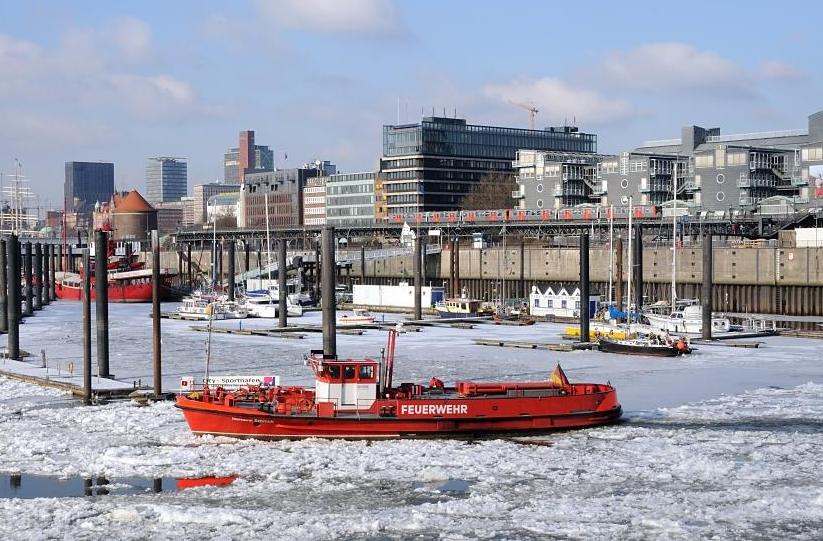 1715 Das Lschboot der Hamburger Feuerwehr hlt als Eisbrecher die Einfahrt zum Hamburger Binnenhafen frei - im Hintergrund der Hamburger City Sportboothafen; einige Sportboote liegen im Eis am Holzsteg. Ein Hochbahnzug fhrt Richtung Haltestelle Baumwall. 