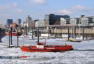 1715 Das Lschboot der Hamburger Feuerwehr hlt als Eisbrecher die Einfahrt zum Hamburger Binnenhafen frei - im Hintergrund der Hamburger City Sportboothafen; einige Sportboote liegen im Eis am Holzsteg. Ein Hochbahnzug fhrt Richtung Haltestelle Baumwall. 