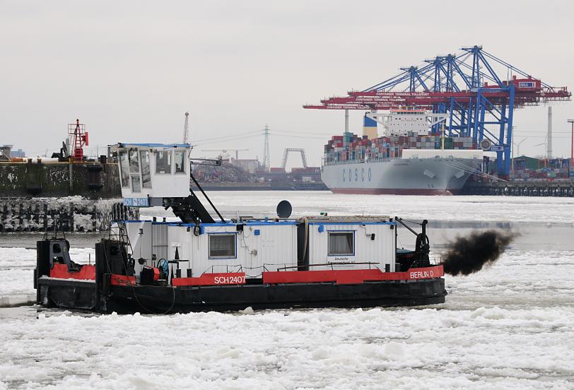 1862 Das Schubschiff SCH 2407 fhrt durch das Treibeis auf der Elbe im Hamburger Hafen; im Hintergrund liegt ein Containerschiff unter den Containerbrcken des Terminals Tollerort.  