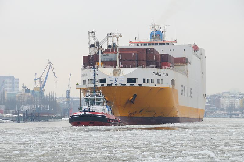 19_6302 Die GRANDE AFRICA, ein RoRo Schiff  (Roll on Roll off) der Grimaldi-Reederei wird durch das dichte Treibeis von einem Schlepper in den Hamburger Hafen geschleppt. Das 214m lange Frachtschiff kann ca. 2500 Fahrzeuge und 800 Container transportieren. Hamburger Winterfotos aus dem Hafen -Frachtschiff mit Schlepper auf der Elbe im Eis.