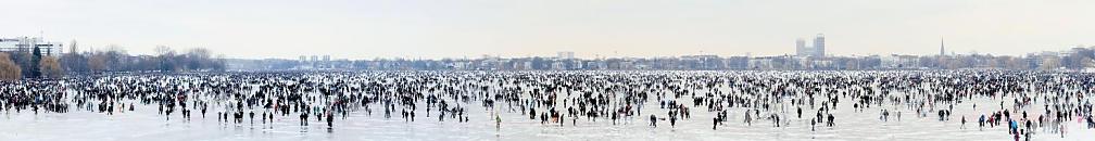 2021_31 Panoramblick auf die zugefrorene Aussenalster - ab einer Strke von 20cm darf das Eis des grossen Hamburger Sees offiziell betreten werden. Es findet das sogenannte Alstereisvergngen statt; Buden mit Glhwein und Wrstchen stehen am Ufer der Alster. Hunderttausende HamburgerInnen und Hamburg-Touristen gehen auf dem zugefrorenen See spazieren, laufen Schlittschuh oder spielen Eishockey. 