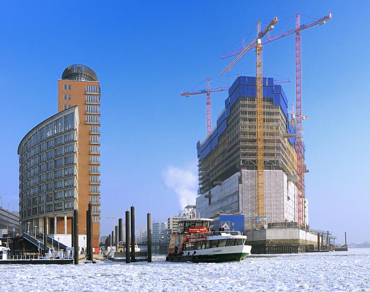 22_5304 Die Elbfhre HAFENCITY verlsst den Anleger am Sandtor; links neben der Einfahrt zum Sandtorhafen der moderne Brokomplex am Kehrwieder und rechts die Hamburger Grossbaustelle der zuknftigen Elbphilharmonie mit den weit sichtbaren Baukrnen.  Hamburg-Motive: die Baustelle der Elbphilharmonie im Winter; Hafenfhre.