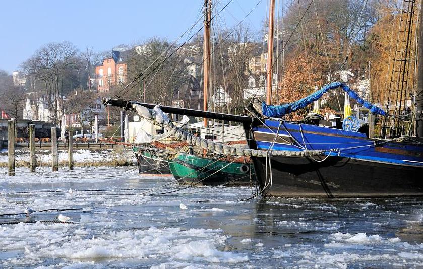 3065 Die historischen Schiffskutter liegen vertut im Museumshafen Oevelgnne - Eis bedeckt das Hafenbecken; die Schiffe sind eingefroren. Hinter den Masten der Kutter die Wohnhuser am Elbstrand von Hamburg Oevelgnne. 