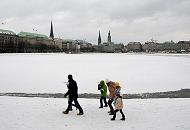 31_4983 Eine Familie geht warm angezogen an einem grauen Wintertag an der Binnenalster spazieren. Im Hintergrund der Rathausturm und die Kirchtrme von St. Petri, St. Nikolai und der St. Michaeliskirche. Hamburgbilder vom Winter - Familienspaziergang an der Binnenalster bei Eis und Schnee.