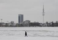 34_4981 An einem grauen Wintertag geht ein einsamer Spaziergnger am Ufer der zugefrorenen Alster spazieren. Am anderen Ufer des 164 ha groen Hamburger Binnensees ragt der Fernsehturm und das Radisson Hotel in den Winterhimmel. Aufnahmen von Hamburger im Winter - grauer Wintertag am Alsterufer.