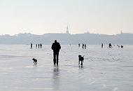 36_5484 Hamburger gehen auf dem Alstereis spazieren und genieen den auergewhnlichen Ausblick. Sie fahren sogar Fahrrad oder nehmen ihre Hunde zum Spaziergang mit aufs Eis. Im Hintergrund der Kirchturm der  Hl. Dreieinigkeitskirche in Hamburg - St. Georg.  Hamburger Winterbilder - Spaziergnger auf dem Eis der Alster vor dem Hamburg Panorama. 
