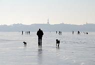 36_5484 Hamburger gehen auf dem Alstereis spazieren und genieen den auergewhnlichen Ausblick. Sie fahren sogar Fahrrad oder nehmen ihre Hunde zum Spaziergang mit aufs Eis. Im Hintergrund der Kirchturm der  Hl. Dreieinigkeitskirche in Hamburg - St. Georg.  Hamburger Winterbilder - Spaziergnger auf dem Eis der Alster vor dem Hamburg Panorama. 