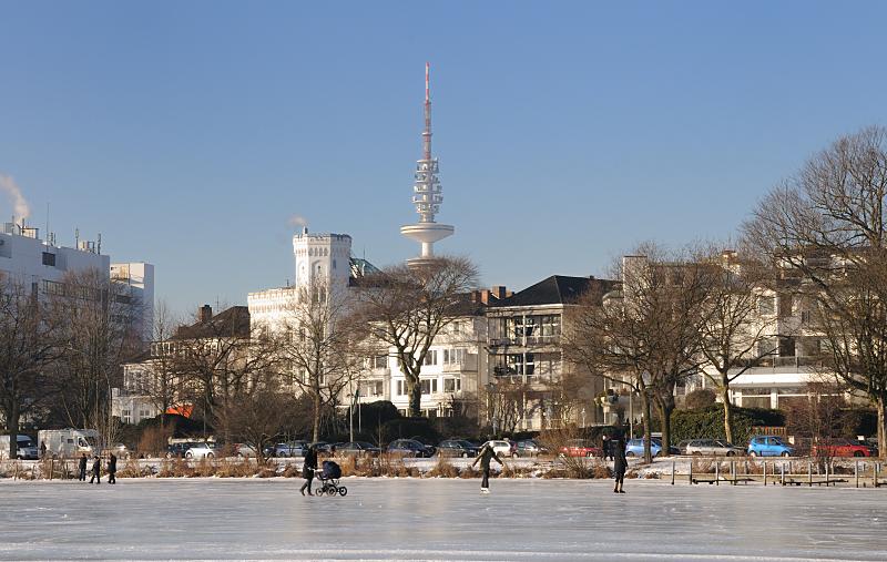 37_5514 Blauer Winterhimmel ber Hamburg - die Aussenalster ist zugefroren. Hamburger und Hamburgerinnen nutzen das schne Winterwetter und gehen auch mit Kinderwagen auf dem Eis spazieren. Andere laufen Schlittschuh auf Hamburgs groem Binnensee. Im Hintergrund historische Hamburger Architektur an der Strasse ALSTERUFER und der Fernsehturm, der zwar den offiziellen Namen Heinrich Hertz Turm hat, aber zumeist Telemichel genannt wird. Hamburger Winterfotos - die zugefrorene Aussenalster mit Spaziergngerinnen auf dem Eis. 