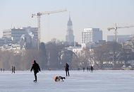 40_5509 Spaziergnger genieen das schne Winterwetter und gehen in der Wintersonne auf der zugefrorenen Alster spazieren. Eine Mutter luft Schlittschuh und zieht dabei ihr Kind auf einem Schlitten. Im Hintergrund der Turm der St. Michaeliskirche.  Hamburger Wintermotive vom Winter 2009 / 2010 - die Hamburger Auenalster ist zugefroren. 