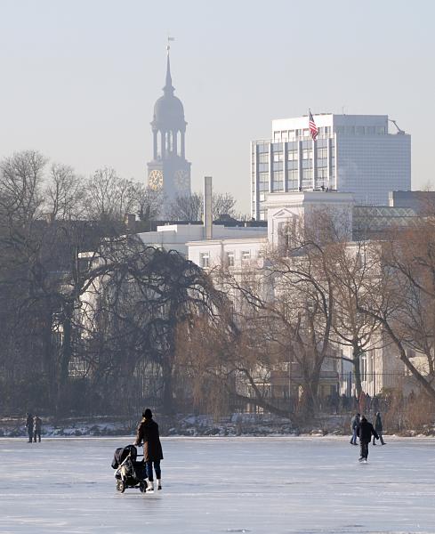 41_5528 Schlittschuhlaufen auf der zugefrorenen Hamburger Aussenalster - eine Mutter schiebt beim Eislauf ihre Kinderkarre. Am Ufer der Alster das Gebude der Amerikanischen Botschaft mit der Flagge auf dem Dach des Hauses; lks. der Kuppelturm des Hamburger Michels. Hamburger Winter - Schlittschuhlaufen auf der Alster. 