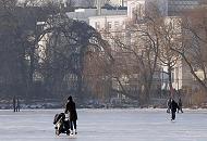 41_5528 Schlittschuhlaufen auf der zugefrorenen Hamburger Aussenalster - eine Mutter schiebt beim Eislauf ihre Kinderkarre. Am Ufer der Alster das Gebude der Amerikanischen Botschaft mit der Flagge auf dem Dach des Hauses; lks. der Kuppelturm des Hamburger Michels. Hamburger Winter - Schlittschuhlaufen auf der Alster. 