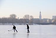 44_5574 Hamburger Jugendliche spielen Eishockey auf der zugefrorenen Alster - hinter der Kennedybrücke sind die Häuser am Jungfernstieg zu erkennen und der Kirchturm der St. Michaeliskirche. Hamburger Jahreszeiten, die Hansestadt im Winter - Eishockeyspieler auf der Außenalster. 