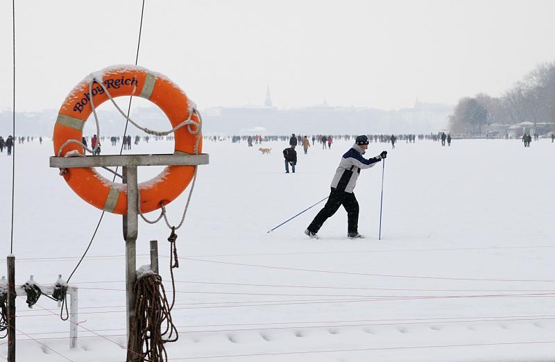 47_6093 Vor dem Anleger des Bootssteg vom Alstercaf Bobby Reich luft ein Hamburger Ski auf der zugefrorenen und verschneiten Alster; ein schneebedeckter Rettungsring hngt am Steg in seiner Halterung. Bilder vom Hamburger Winter - Langskilaufen auf der verschneiten Alster.