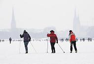 48_6109 Skilangläuferinnen nutzen den hohen Schnee auf dem Alsterei, um eine Runde um den 164 ha großen Binnensee zu machen; die Rundstrecke am Alsterufer ist für Jogger ca. 7,5 km lang. Im Hintergrund in den Schneewolken die Kirchtürme der St. Petri und Nikolaikirche sowie rechts der Rathausturm. Fotos vom Hamburger Winter - HamburgerInnen machen Skilanglauf auf der Alster.