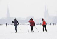 48_6109 Skilangluferinnen nutzen den hohen Schnee auf dem Alsterei, um eine Runde um den 164 ha groen Binnensee zu machen; die Rundstrecke am Alsterufer ist fr Jogger ca. 7,5 km lang. Im Hintergrund in den Schneewolken die Kirchtrme der St. Petri und Nikolaikirche sowie rechts der Rathausturm. Fotos vom Hamburger Winter - HamburgerInnen machen Skilanglauf auf der Alster.