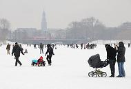 49_6117 Die Hamburgerinnen und Hamburger genieen mit ihren Kinder das Alstereisvergngen -sie ziehen ihre Sprsslinge auf Schlitten ber das Eis oder schieben ihren Kinderwagen ber die Alster. Im Hintergrund der Michelturm - ber die Lombardsbrcke fhrt ein Zug. Winterbilder aus Hamburg - Winterspass im Schnee auf der zugefrorenen Alster.