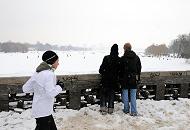 52_6076 Von der Krugkoppelbrücke hat man einen weiten Blick über die weiße, zugefrorene Alster - die Hamburger nutzen das Wintereis, um quer über die Alster in die Hamburger Innenstadt zu spazieren. Andere joggen an Land durch den Schnee die 7,5 km um Alster herum. Aufnahmen von Hamburg im Winter - Blick von der Krugkoppelbrücke auf die Alster, Joggerin. 