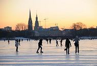 56_5925 Bis in den Abend hinein nutzen die Hamburger und Hamburgerinnen die Mglichkeit auf der zugefrorenen Auenalster Schlittschuh zu laufen oder spazieren zu gehen. Im Sonnenuntergang zeichnen sich Baukrne und der Turm des Rathauses und der Nikolaikirche im roten Abendhimmel ab. Winterliches Hamburg - Alstereisvergngen auf der Aussenalster; Sonnenuntergang.