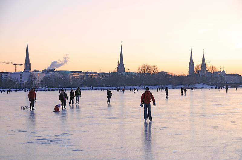 57_5906 Vor dem Hamburg-Panorama mit den markanten Kirchtrmen berqueren die Hamburger auf dem Eis der Aussenalster den 156 ha groen Hamburger Binnensee. Offiziell wird die Alster erst von der Behrde freigegeben, wenn das Eis eine Strke von 20cm hat, aber viele Hamburger laufen schon vorher z.B. mit ihren Schlittschuhen oder Schlitten ber das Eis.  Bilder vom winterlichen Hamburg - Alstervergngen bei Minustemperaturen auf der Aussenalster.