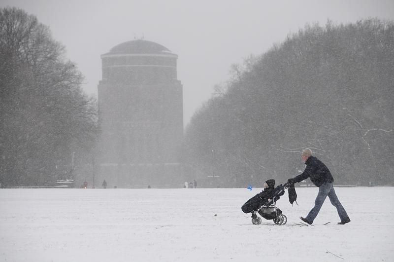 63_5054 Der Schnee fllt in dichten Flocken im Stadtpark von Hamburg Winterhude - ein junger Vater schiebt die Karre mit seinem Kind ber den schneebedeckten Fuweg auf der groen Stadtparkwiese.  Bilder vom Hamburger Winter - Spaziergnger und Schneefall im Winterhuder Stadtpark.