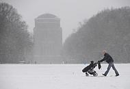 63_5054 Der Schnee fllt in dichten Flocken im Stadtpark von Hamburg Winterhude - ein junger Vater schiebt die Karre mit seinem Kind ber den schneebedeckten Fuweg auf der groen Stadtparkwiese.  Bilder vom Hamburger Winter - Spaziergnger und Schneefall im Winterhuder Stadtpark.