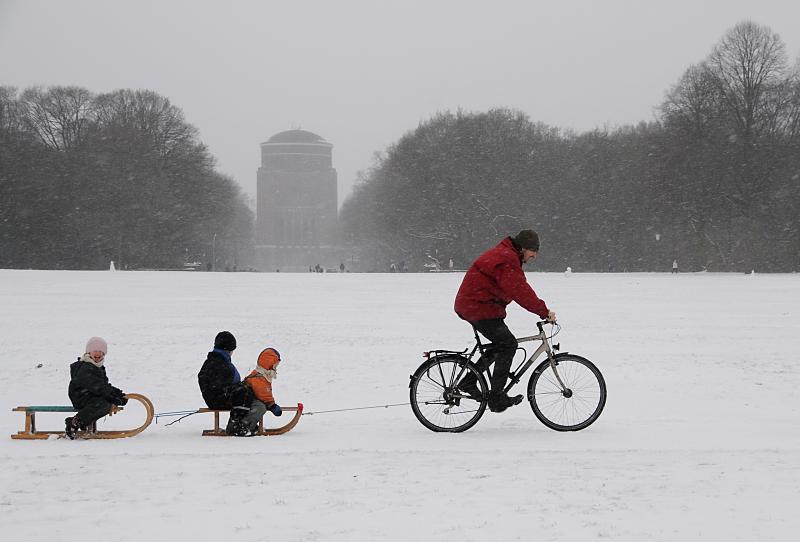 64_5069 Der Hamburger Stadtpark ist eingeschneit. Ein Vater zieht mit seinem Fahrrad die zwei Schlitten seiner Kinder durch den Schnee ber die groe Wiese. Bilder vom Winter in der Hansestadt Hamburg - Winterfreuden im Hamburger Stadtpark.
