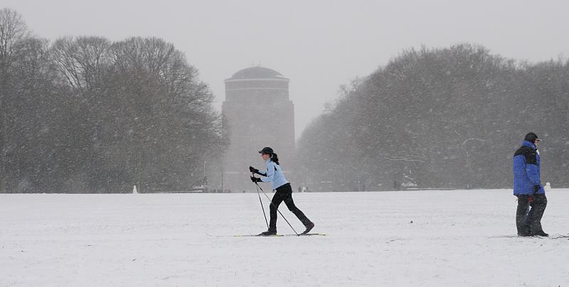 65_5059 Die groe Wiese im Zentrum des Stadtparks ist zugeschneit. Eine Skilangluferin fhrt durch den winterlichen Stadtpark, whrend ein Spaziergnger dick verpackt durch das Schneetreiben stapft.  Im Hintergrund das Hamburger Planetariums. Der ehemalige Wasserturm wird seit 1930 als Planetarium genutzt. Bilder vom Winter in der Hansestadt Hamburg - Schneetreiben und Skilanglauf im Stadtpark.