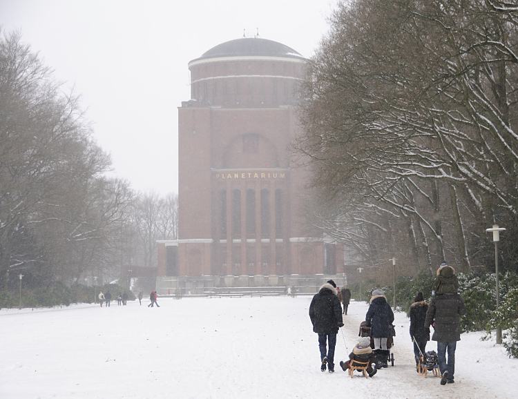 66_5083 Familien gehen im Schnee des Hamburger Stadtparks spazieren - Vter ziehen ihre Sprsslinge auf dem Schlitten oder tragen sie Huckepack, eine Mutter schiebt ihren Kinderwagen durch den Schnee auf dem Weg zum Planetarium. Der Schriftzug steht in goldfarbenen Buchstaben an der Fasse des 78m hohen Gebudes. Fotos vom Winter in der Hansestadt Hamburg - Familienspaziergang im winterlichen Stadtpark.