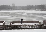 68_5042 An einem grauen Wintertag geht ein Paar am Stadtparksee spazieren - sie schtzen sich miti einem Schirm gegen den Schneefall. Auf dem fast zugefrorenen See sitzen Mwen auf dem dnnen Eis. Im Hintergrund das Freibad Stadtparksee. Fotos von Hamburg im Winter - Grauer Wintertag am Stadtparksee, Spaziergnger.